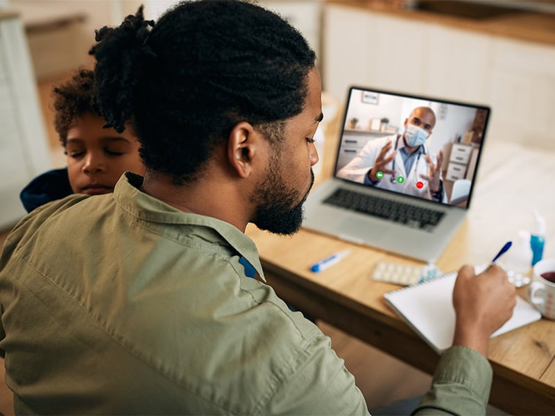 African-American-father-taking-notes-while-having-video-call-with-family-doctor-at-home