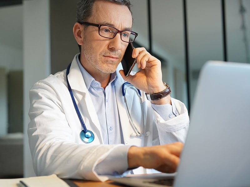 Doctor-in-office-working-on-laptop-talking-on-phone