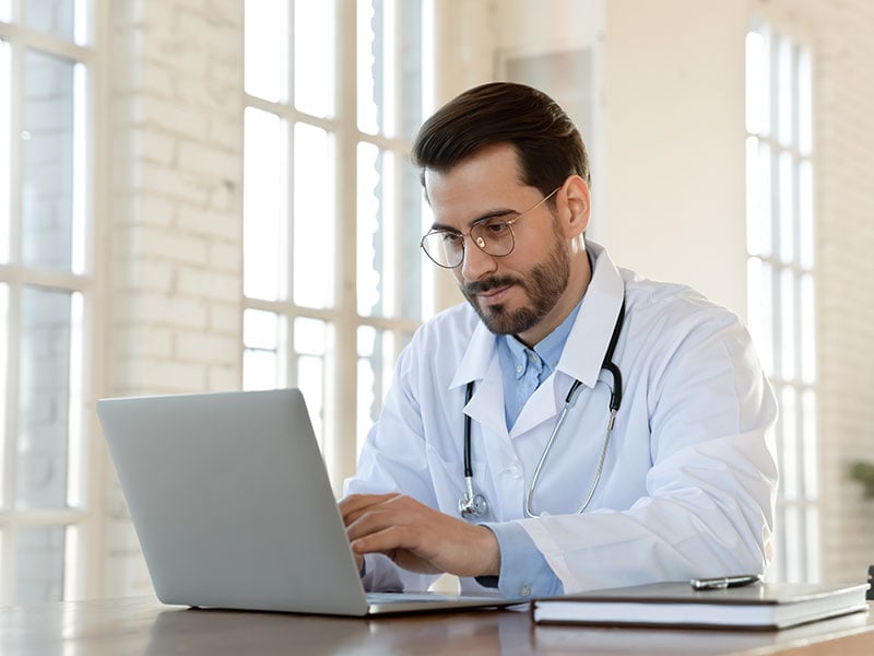 Focused-young-doctor-wearing-glasses-working-on-laptop-in-office