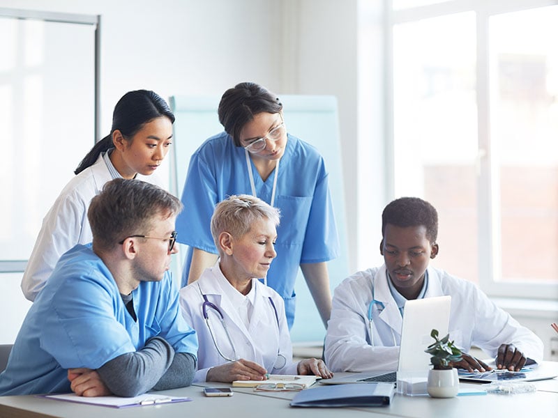 Multi-ethnic-group-of-doctors-looking-at-laptop-screen-while-working-together-sitting-at-desk-in-medical-office-interior