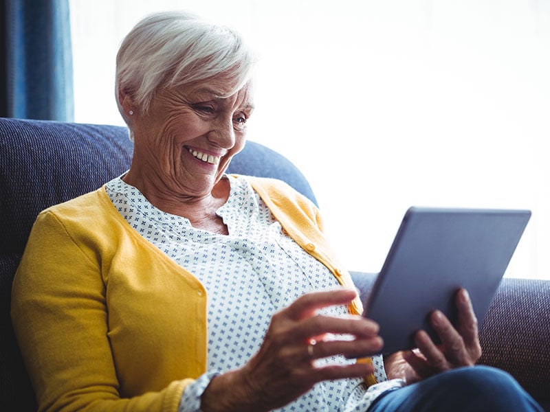 Smiling-senior-woman-looking-and-laughing-at-her-digital-tablet