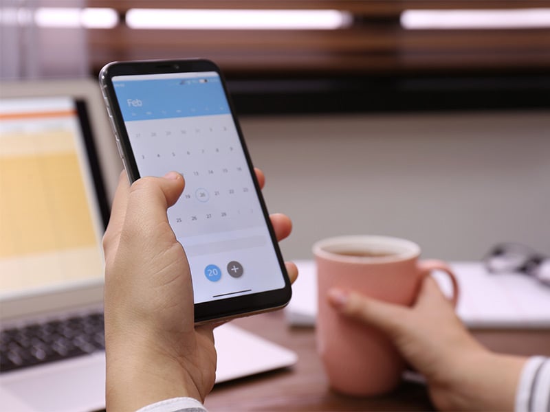 Woman-holding-smartphone-with-calendar-app-at-table