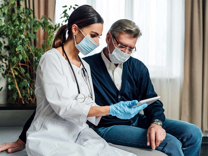 A-nurse-in-a-protective-mask-consults-an-older-man-at-home