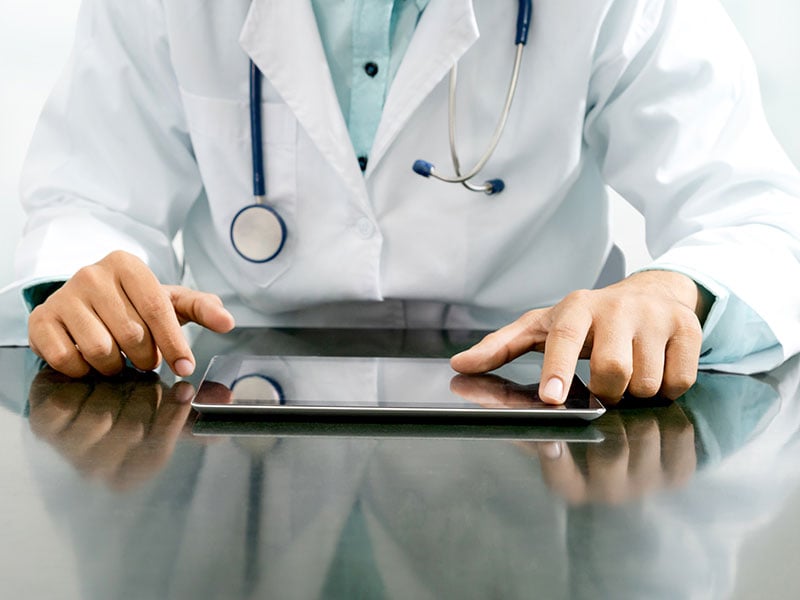 Male-doctor-sitting-at-table-with-tablet-computer-in-hospital-office